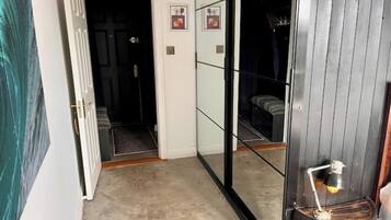 A hallway with a mirrored wall, a door leading to a dark room, and a small table with a lamp.