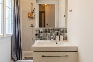 Een badkamer met een douche, een wastafel met spiegel en een betegelde spatwand.