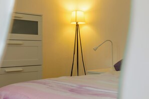 Een slaapkamer met een bed, nachtkastje, lamp en een kledingkast.