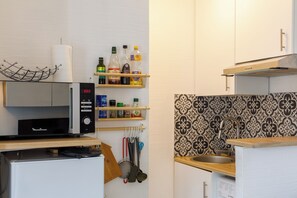 A compact kitchen with a built-in microwave, a coffee machine, and a variety of kitchen utensils and bottles on shelves. - Centrally-Located 1BD Flat—Clignancourt (Paris)