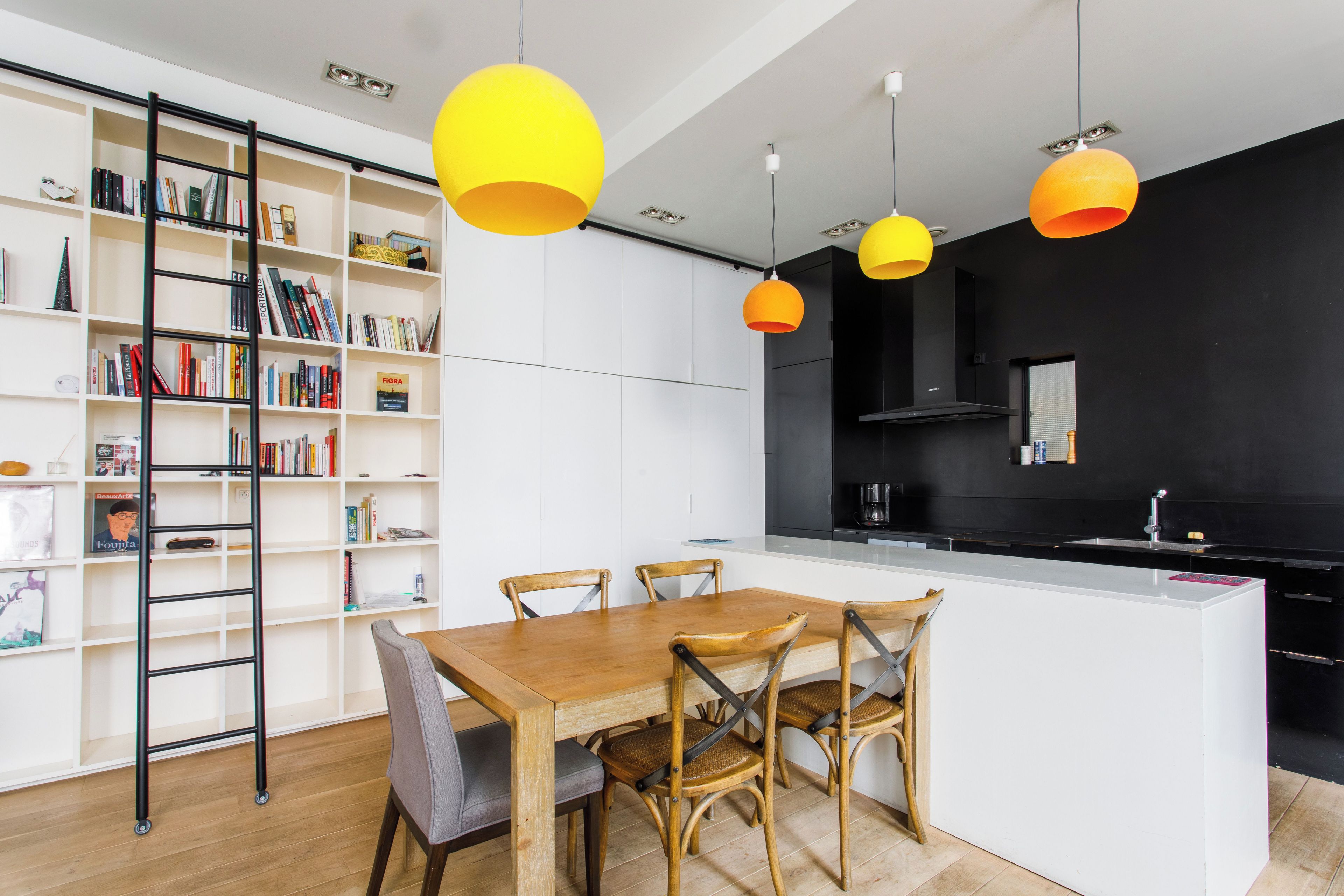 A modern kitchen with a central island, wooden chairs, and a bookshelf filled with books.