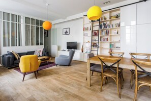 Una sala de estar moderna con un sofá, una mesa de centro, una mesa de comedor con sillas, una estantería y un televisor.