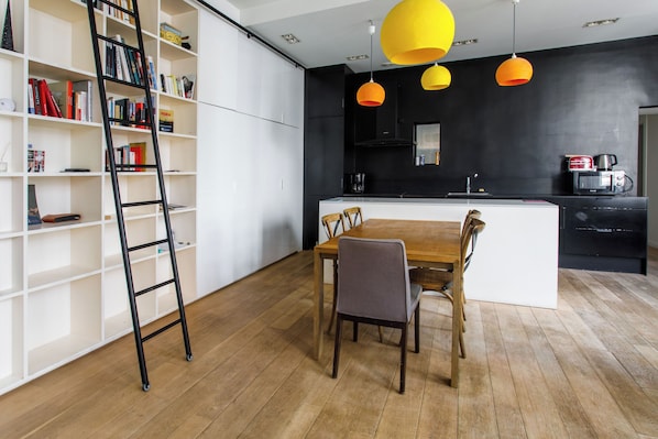 Una cocina moderna con una isla central, una mesa de comedor con sillas y una estantería con escalera.