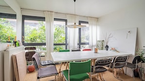 A dining area with a large table, several chairs, and a view of greenery outside. - Stunning 3BD Industrial-style Maisonette—Villette (Paris)