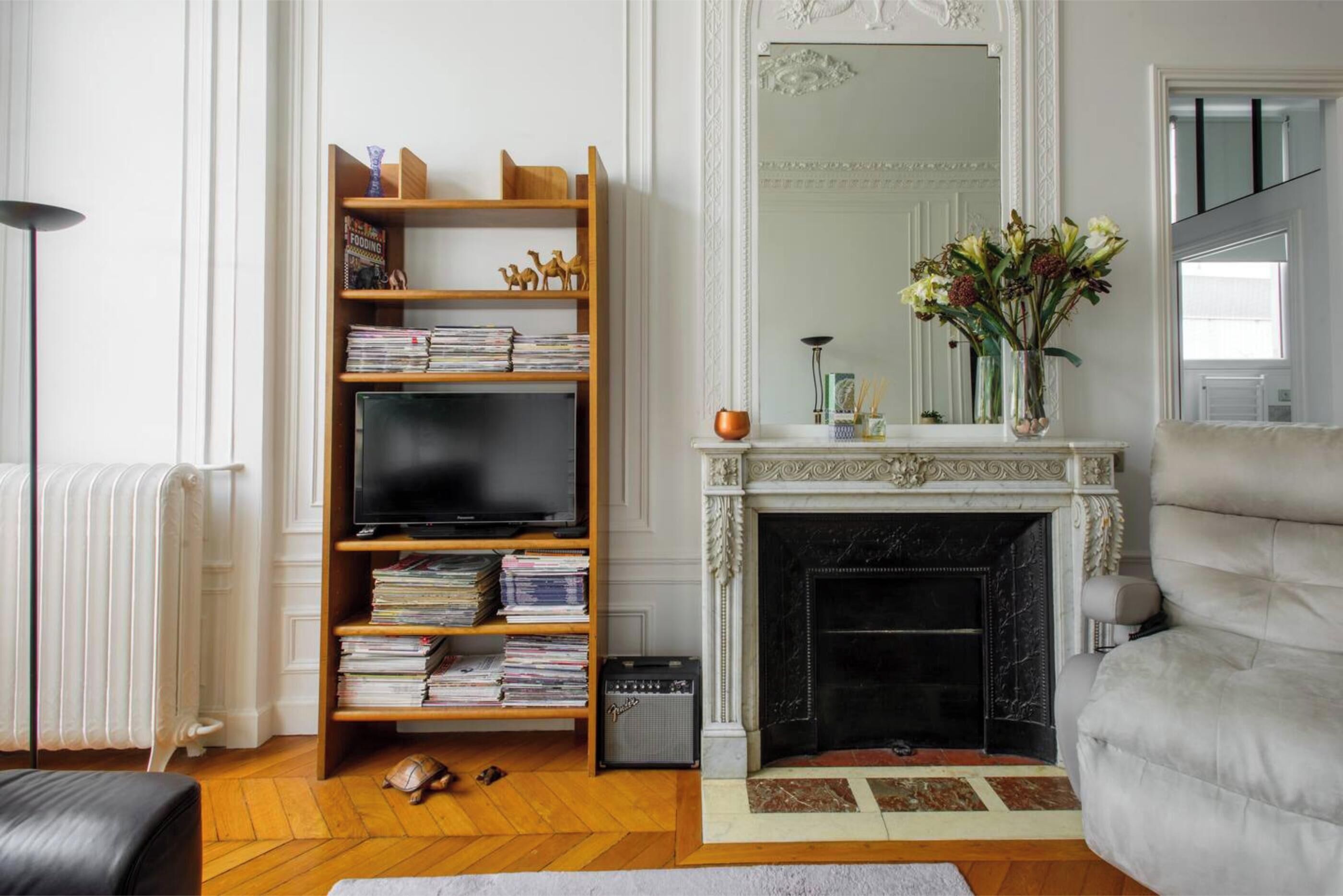 Ein Wohnzimmer mit Kamin, Bücherregal, Fernseher und Heizkörper.