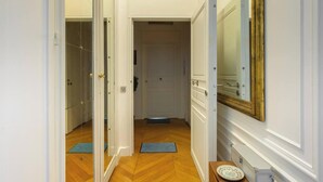 A hallway with a wooden floor, a door leading to a room, a mirror on the wall, and a small table with a plate. - Beautiful 1BD Apartment—Porte Dauphine (Paris)