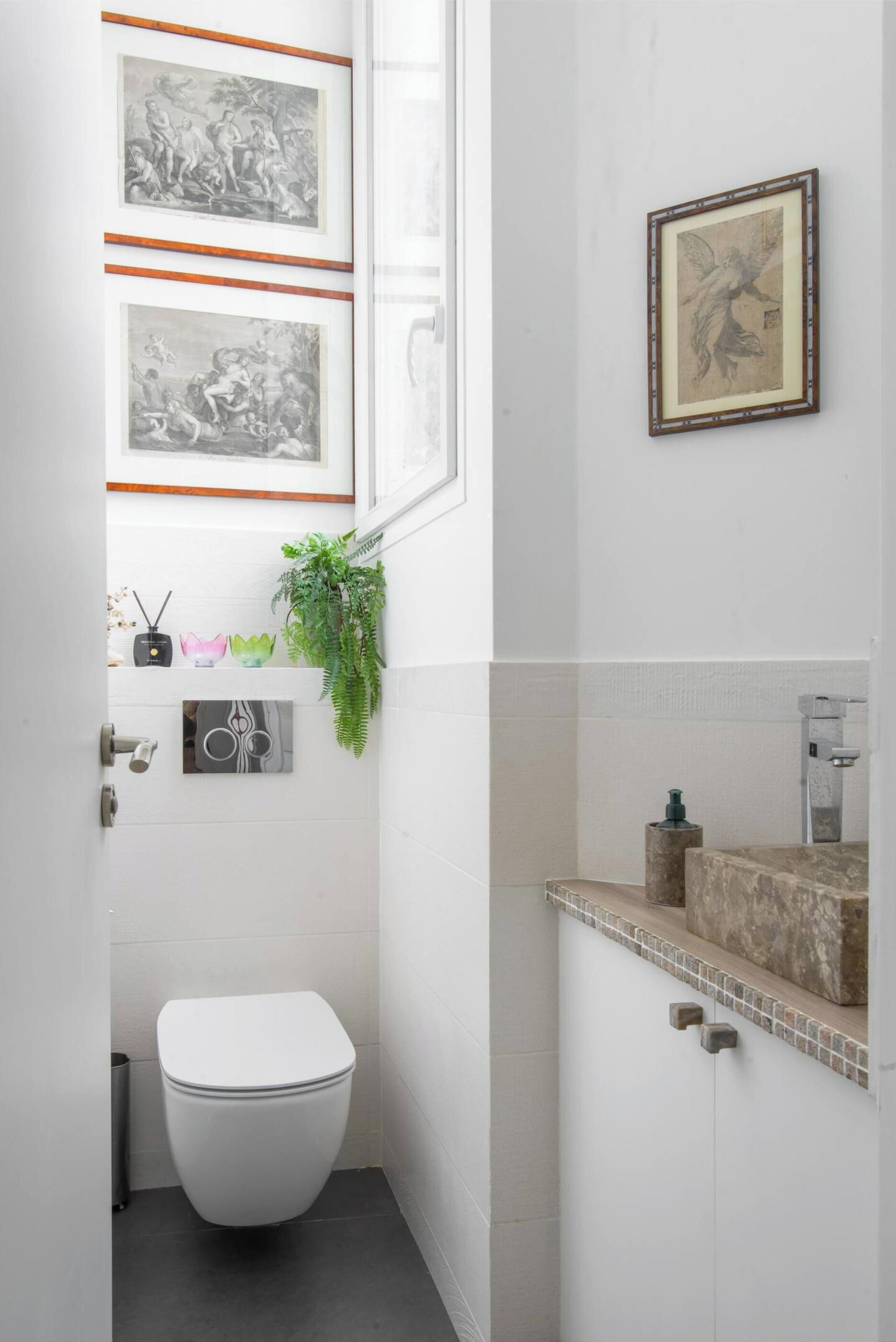 A compact bathroom with a white toilet, a small sink with a stone countertop, and framed artwork on the walls.