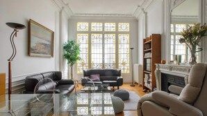 A living room with a glass coffee table, two sofas, a fireplace, and a large window with decorative glass panes. - Beautiful 1BD Apartment—Porte Dauphine (Paris)