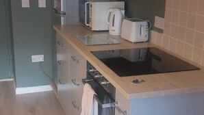 A compact kitchen with a microwave, toaster, and kettle on the counter, a built-in oven, and a stainless steel refrigerator. - Cozy Basement Gem in Top Area (Dublin)