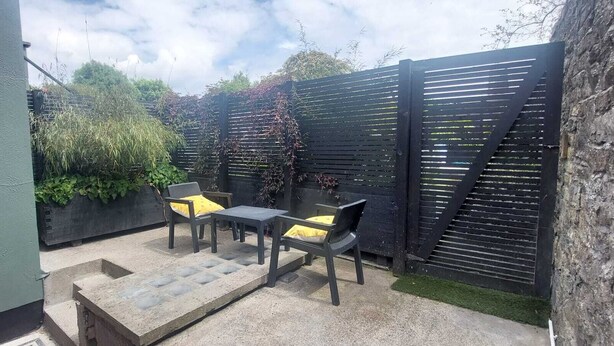 A patio with two tables and chairs, a stone bench, and a black fence. - Cozy Basement Gem in Top Area (Dublin)