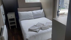 A neatly made bed with white linens and towels, a bedside table, and a window with a view of the outside. - Cozy Basement Gem in Top Area (Dublin)