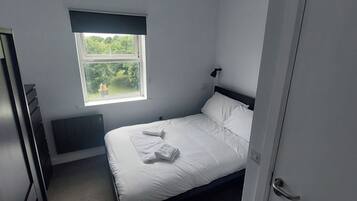 Un dormitorio con una cama individual, un ventanal con vistas a la vegetación y una puerta.