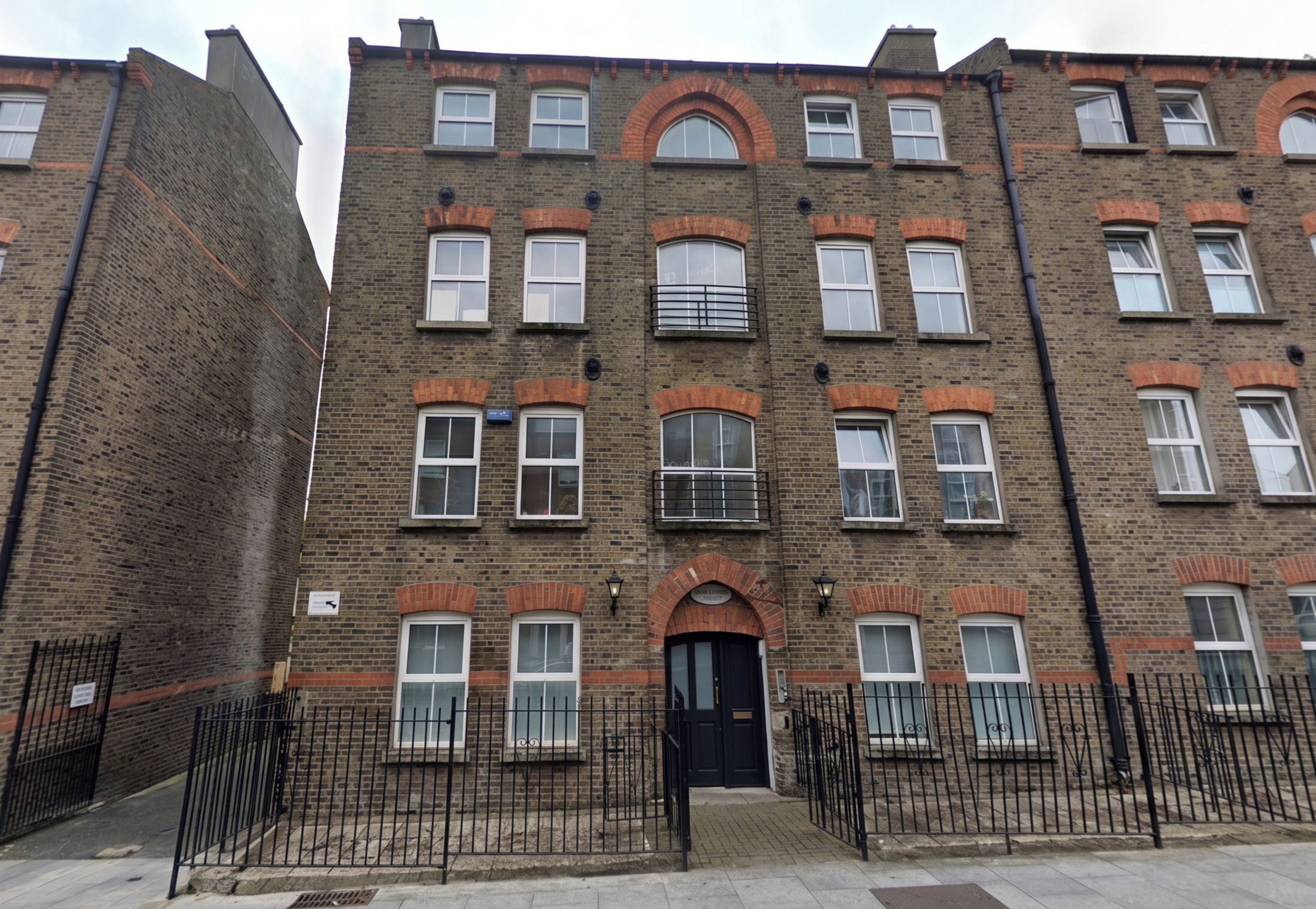 A multi-story brick building with a symmetrical facade, multiple windows, and a central entrance with a black door.