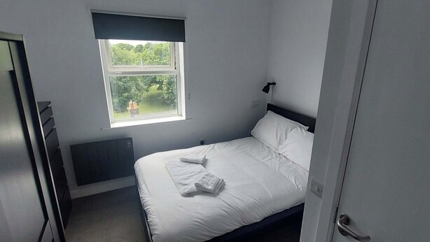 Una habitación pequeña con cama individual, ventana, radiador y puerta.