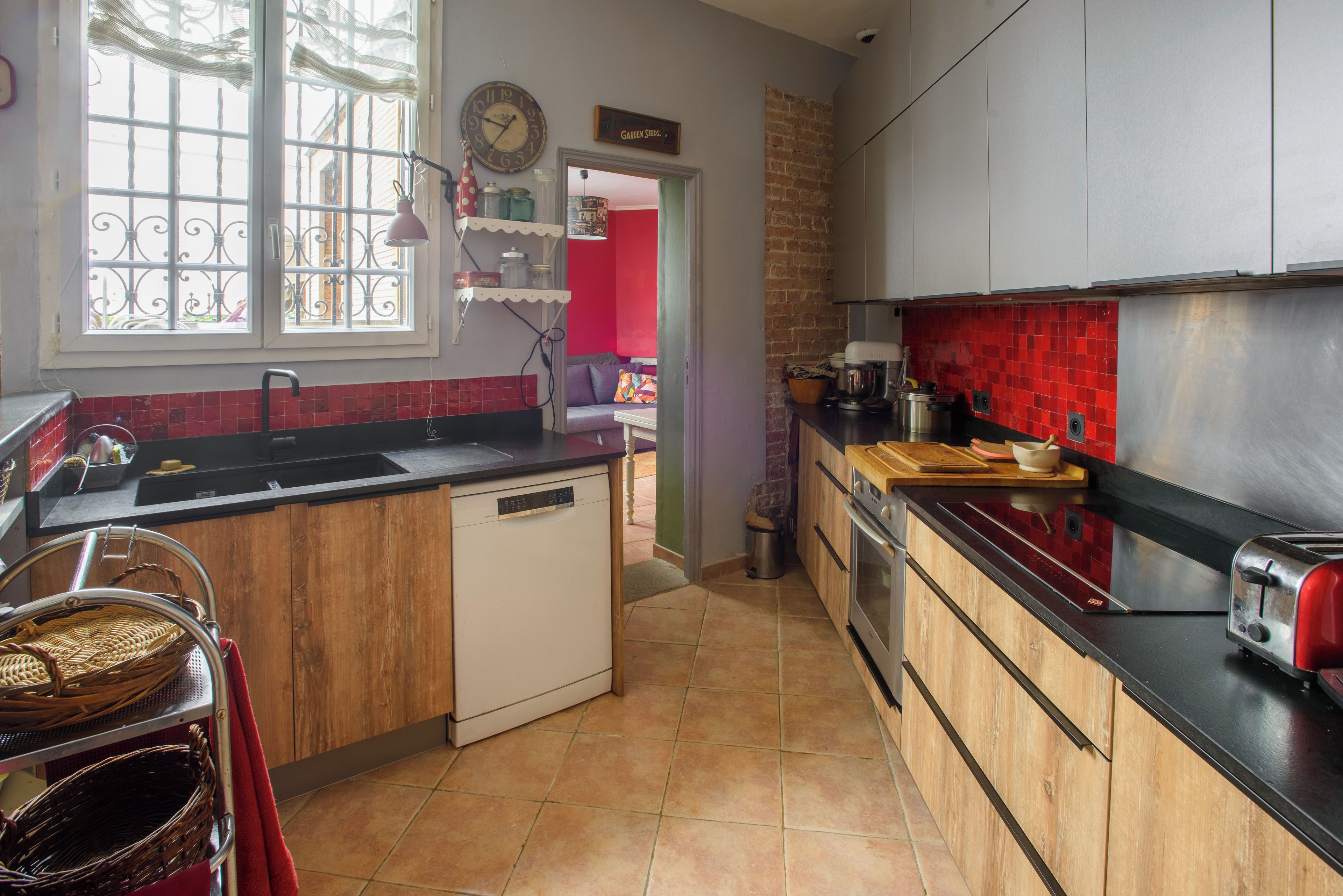 A kitchen with a dishwasher, a sink, a toaster, and a red tiled backsplash.