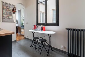Une cuisine avec un plan de travail blanc, deux tabourets noirs, une bouilloire rouge et un radiateur noir.