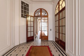 Un couloir doté d’un sol carrelé, d’un tapis rouge et de portes en bois avec des panneaux de verre.