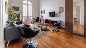 Un salon spacieux avec une grande fenêtre, un canapé, une table basse, un téléviseur et un plancher en bois.