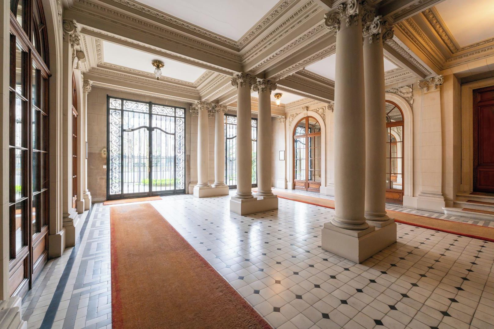 Un vaste hall d’entrée orné de grandes colonnes, doté d’un tapis rouge et d’un sol carrelé.
