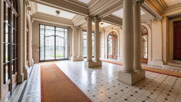 Un vaste hall d’entrée orné de grandes colonnes, doté d’un tapis rouge et d’un sol carrelé.