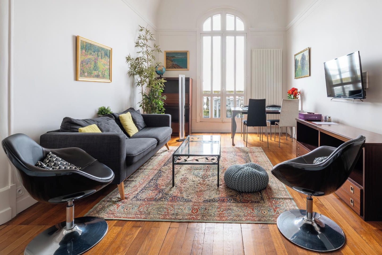 Een ruime woonkamer met een donkergrijze bank, twee zwarte fauteuils, een salontafel en een groot raam met uitzicht op de omgeving.
