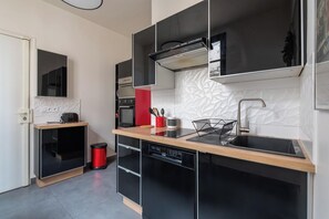Une cuisine moderne avec des meubles de couleur noire, un plan de travail en bois, un four encastré, un lave-vaisselle et une poubelle rouge.