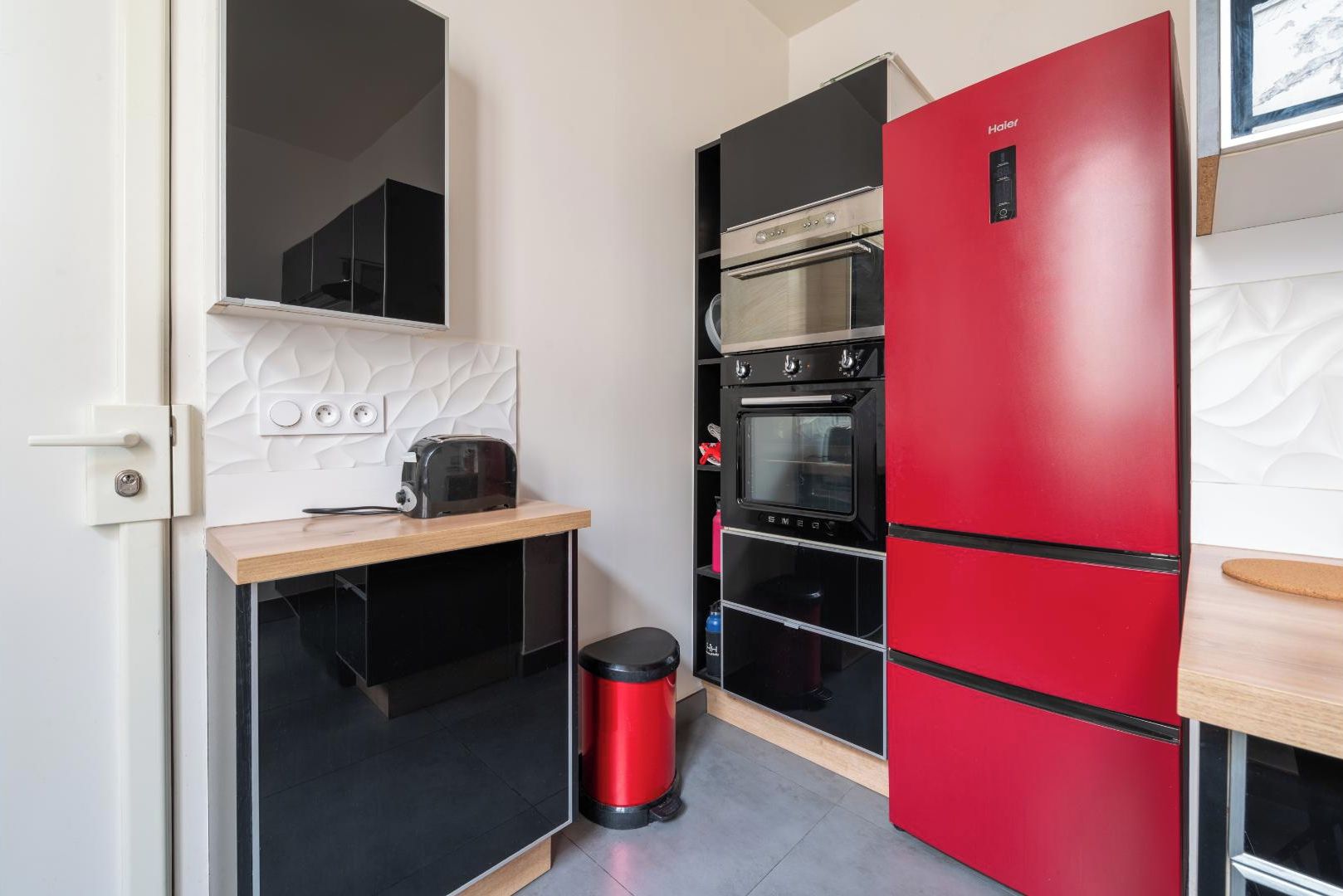 Een kleine keuken met een rode koelkast, een inbouwoven en een broodrooster op een houten aanrecht.