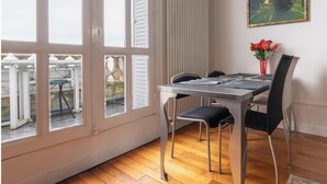 Un coin repas avec une table et des chaises, une fenêtre avec des volets et un tableau accroché au mur.