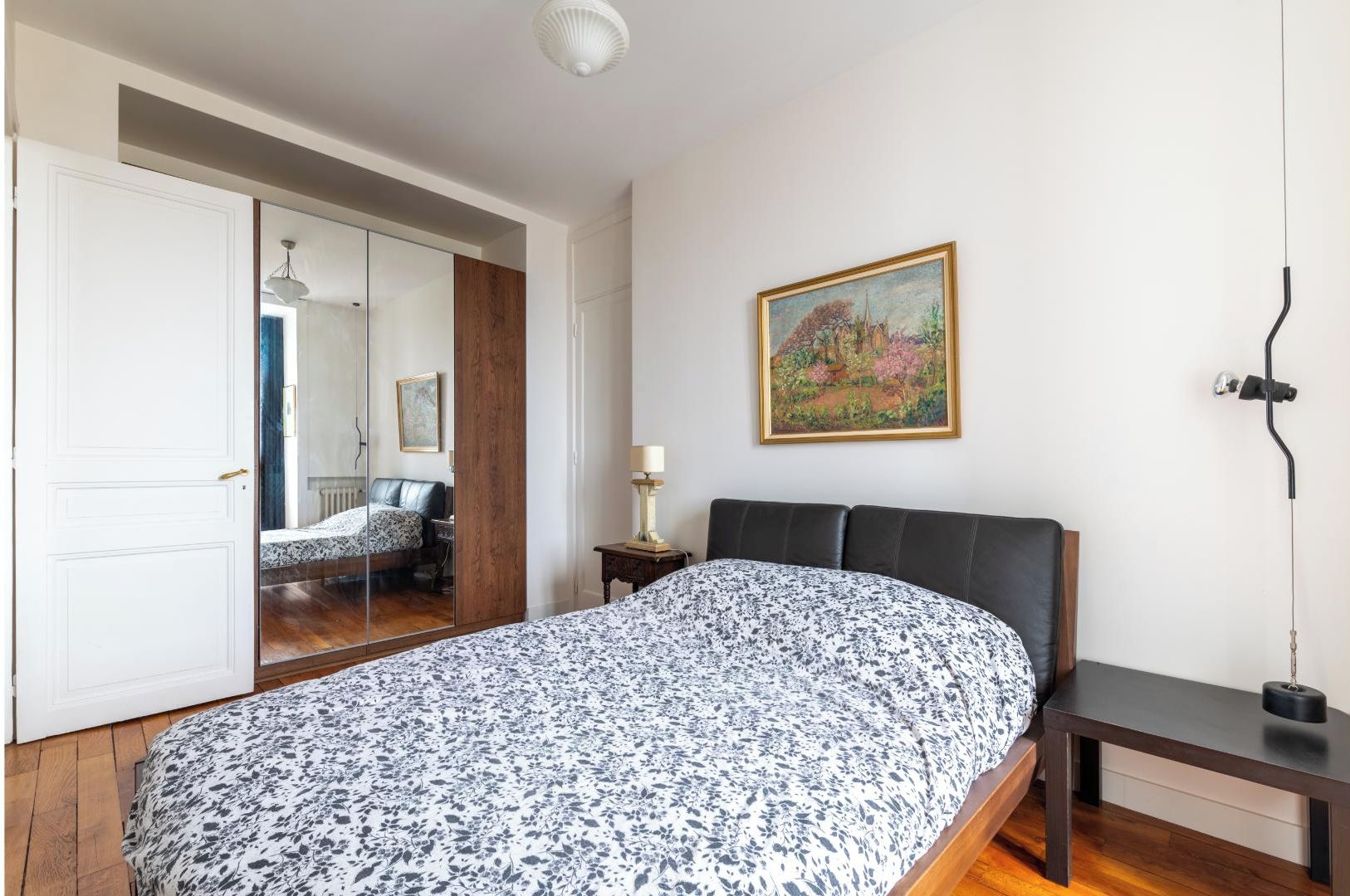 Une chambre à coucher avec un lit, une table de chevet, une lampe, un tableau et une armoire.