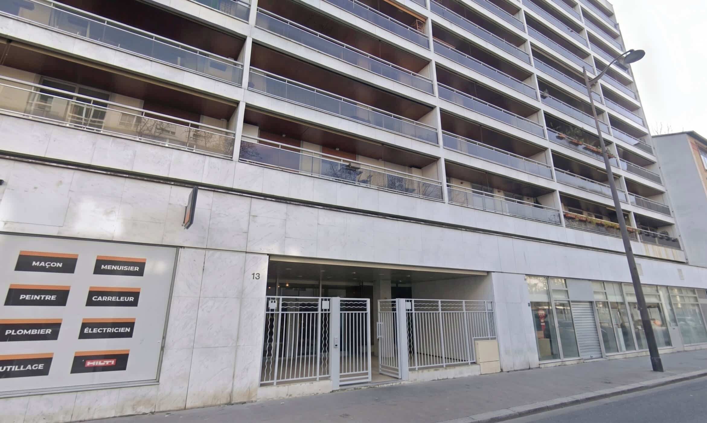 Un edificio de varios pisos con balcones y una entrada a nivel de calle con una reja de metal.