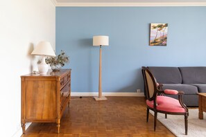 Una habitación con un aparador de madera, una lámpara de pie, un sofá gris y una silla con cojín rosa.