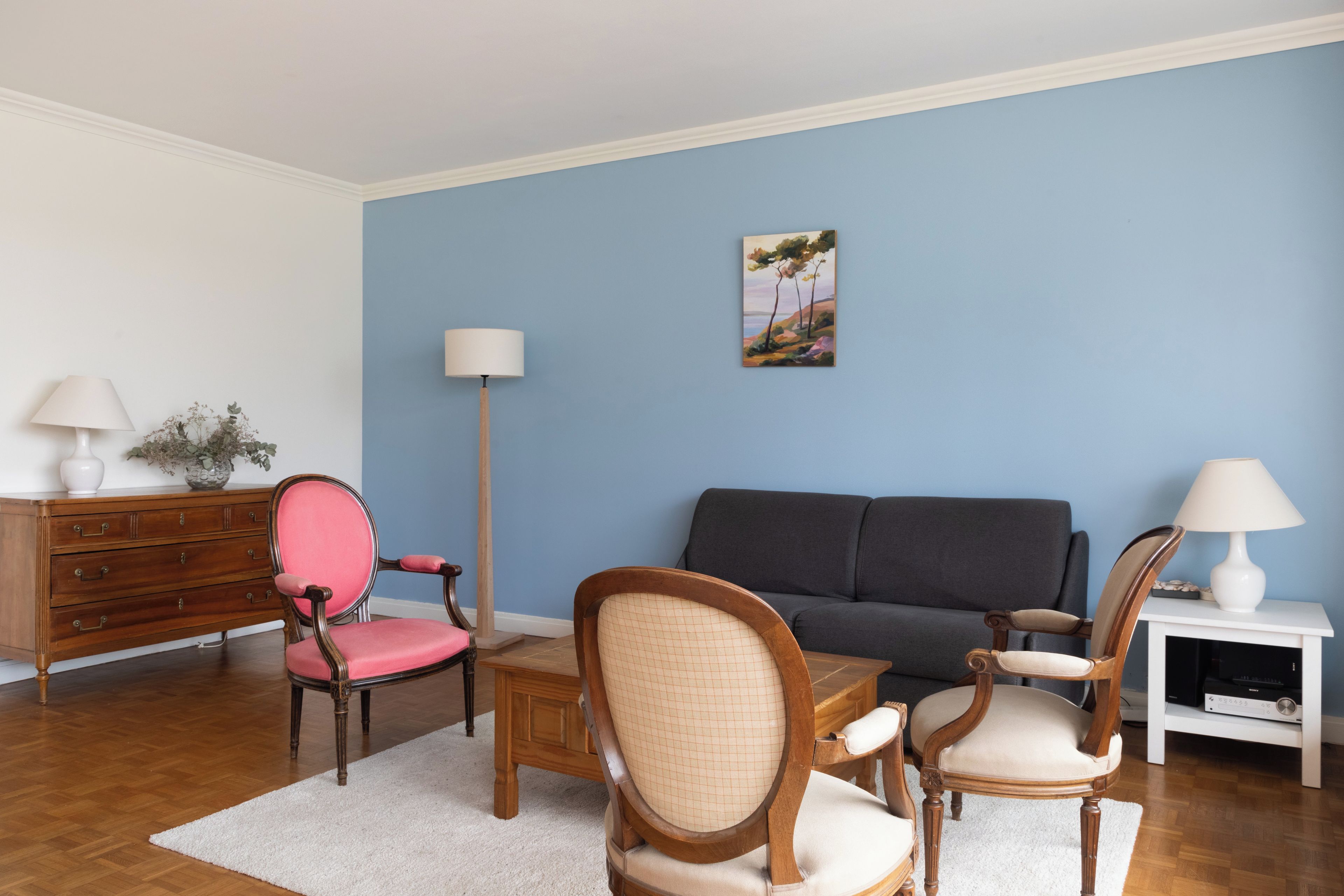 A living room with a sofa, two chairs, a coffee table, a lamp, a dresser, and a painting on the wall.