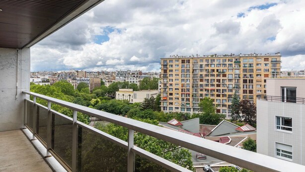 Un balcón con vista a una zona residencial, que incluye un edificio de varios pisos con balcones y diferentes construcciones.