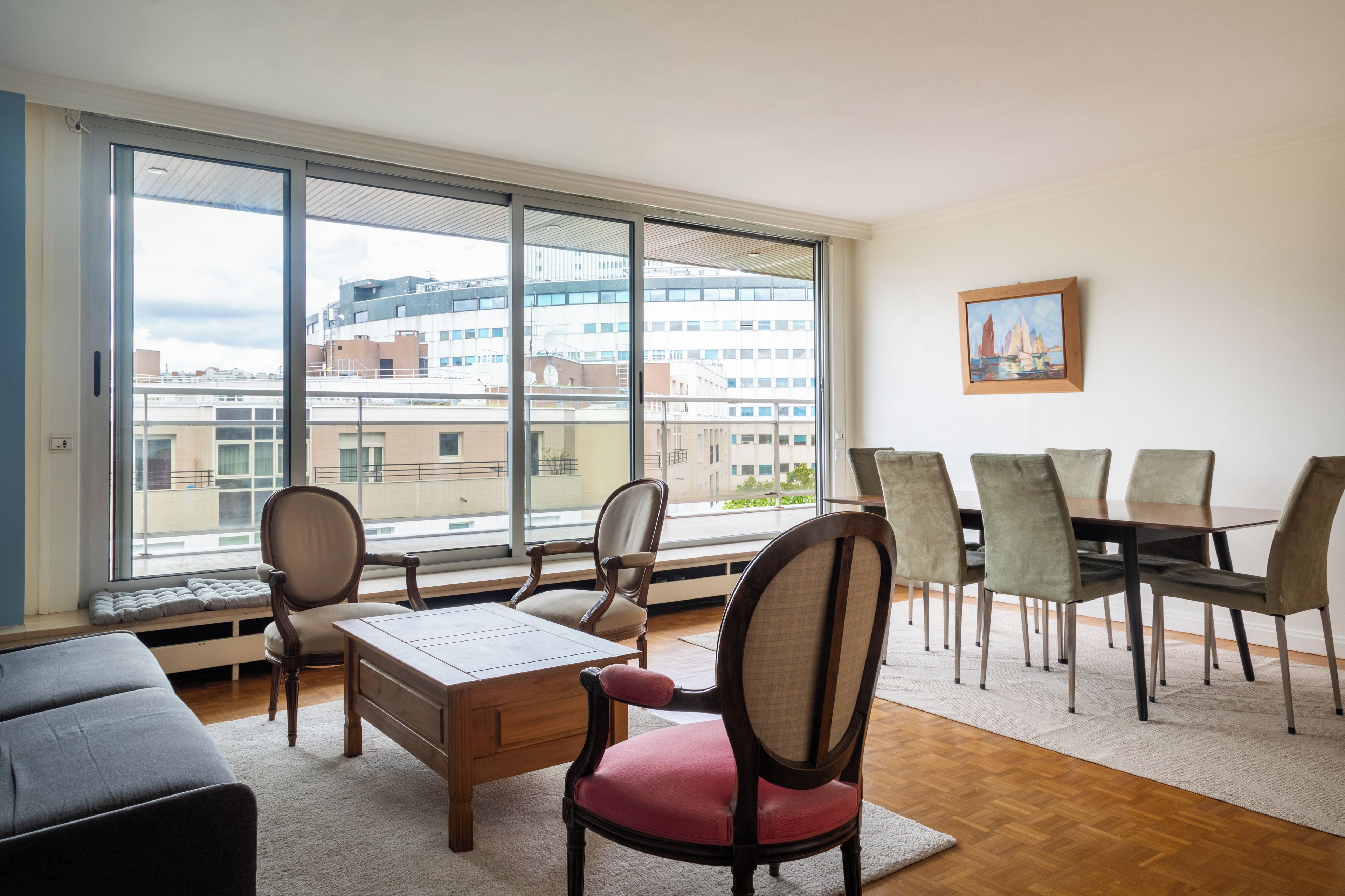 A spacious living area with a large window, a dining table with chairs, and a cozy seating area.