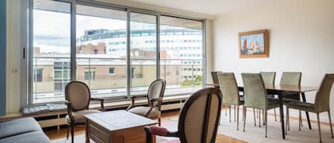 A spacious living area with a large window, a dining table with chairs, and a cozy seating area.