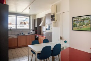 Une cuisine compacte avec un coin repas, dotée d’une fenêtre offrant une vue sur la ville, d’un four à micro-ondes encastré et d’une table rouge.