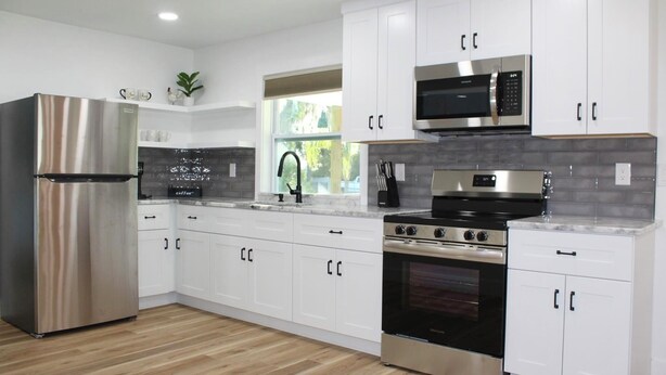 A modern kitchen with stainless steel appliances, white cabinetry, and a window providing natural light.