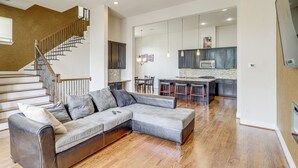 A spacious living area with a large sectional sofa, a wooden staircase, and a modern kitchen in the background. - Houston Home w/ Rooftop Patio - 3 Mi to Downtown! (Houston)