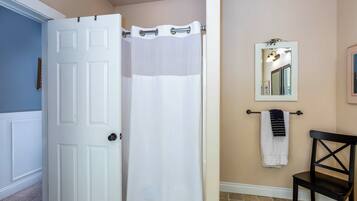 A bathroom with a white door, a shower curtain, a towel rack with a towel, a mirror, and a chair.