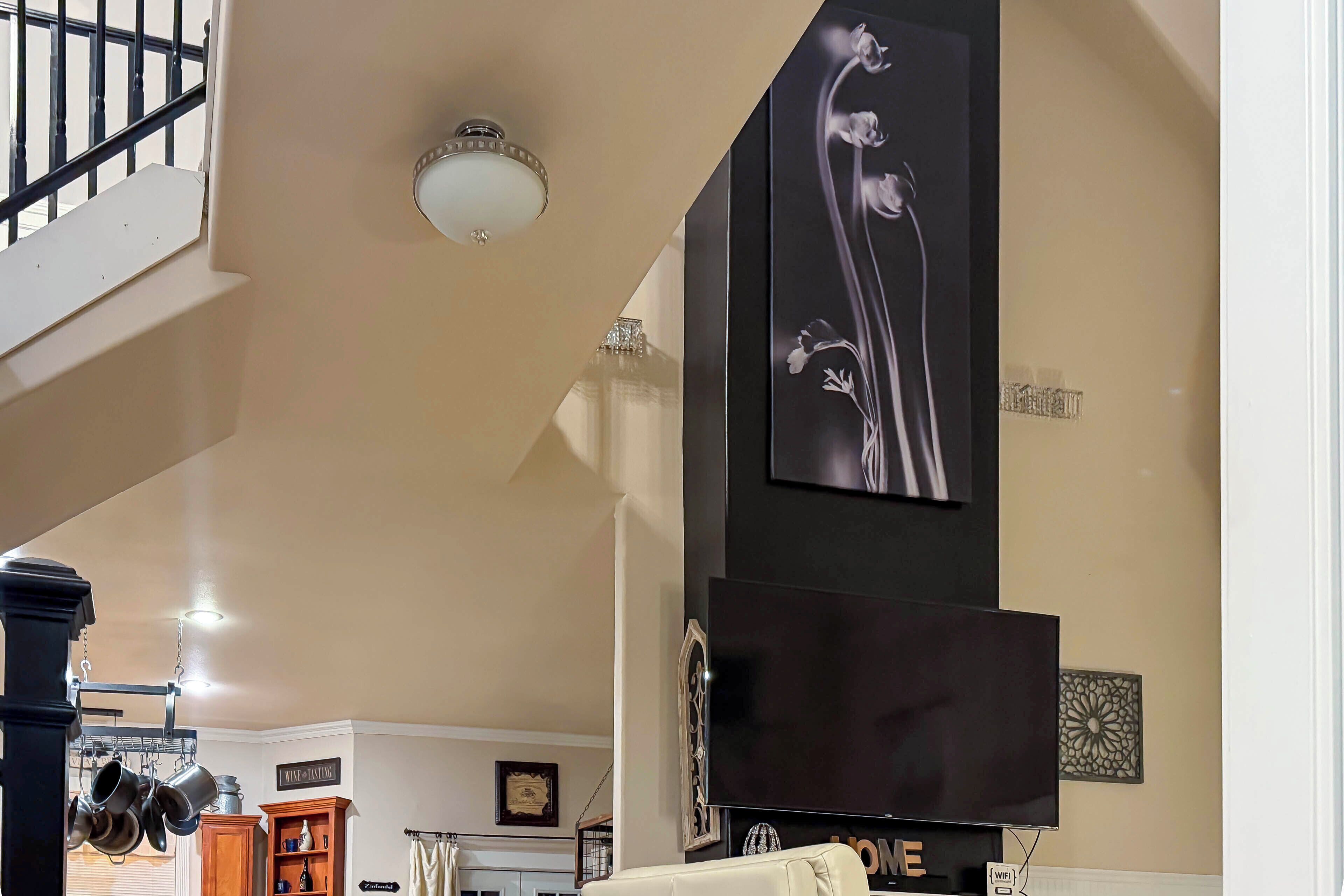 A living room with a staircase, a flat-screen TV, and a decorative wall piece.
