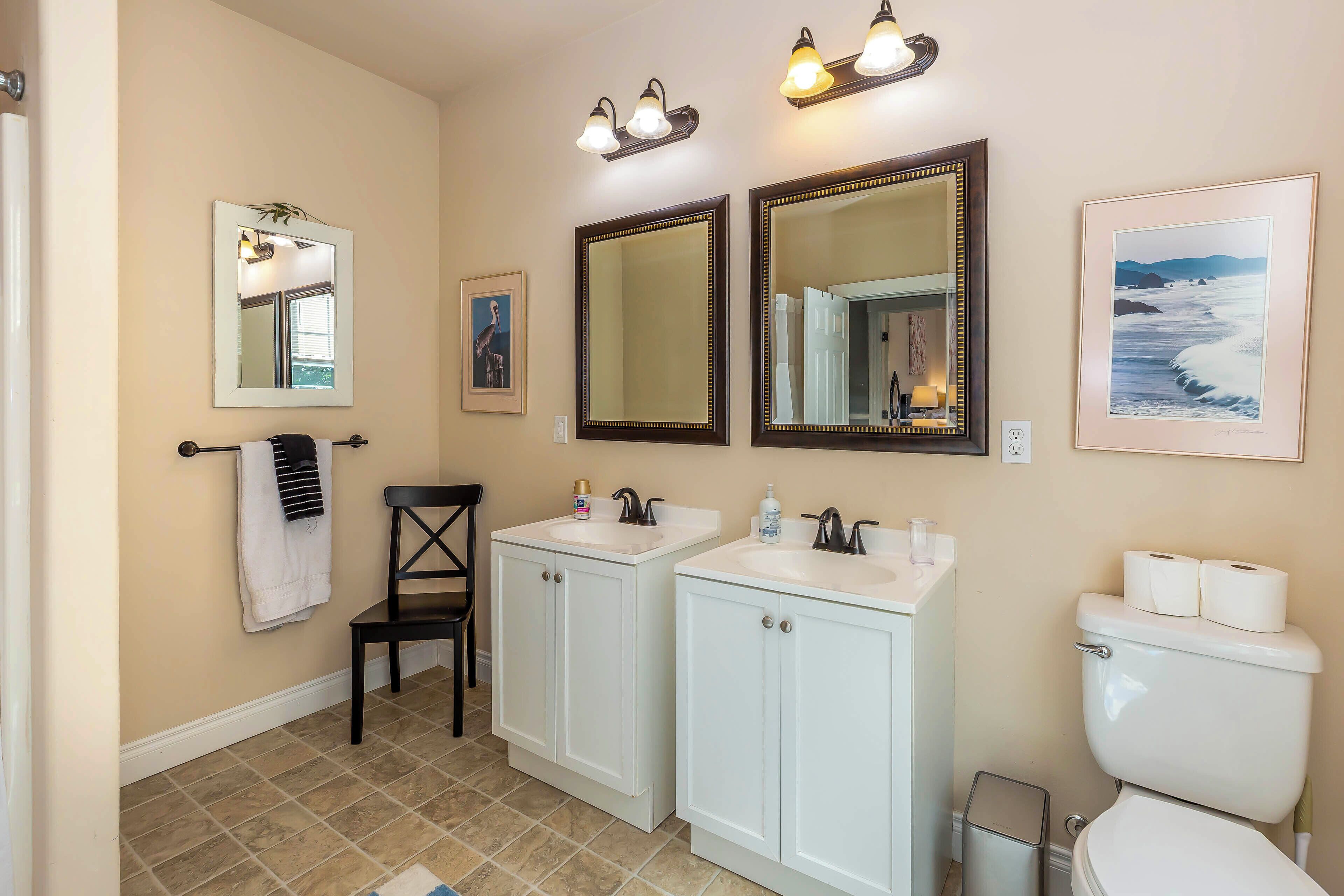 A bathroom with two sinks, a toilet, a chair, and mirrors.