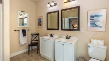 A bathroom with two sinks, a toilet, a chair, and mirrors.