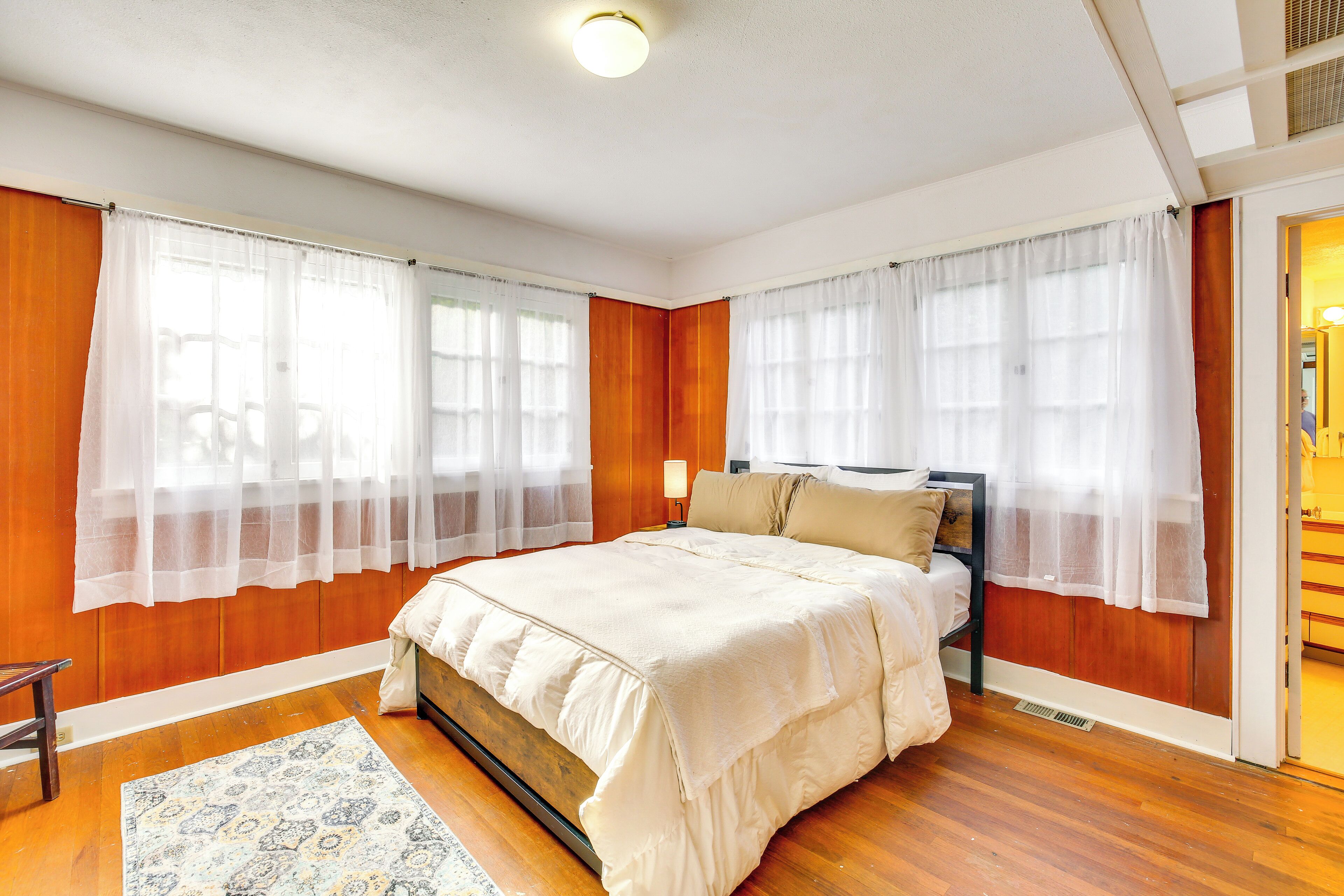 Un dormitorio con pared de paneles de madera, una cama con colcha color beige, dos mesitas de noche y un tocador.