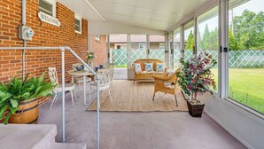 En overdækket terrasse med murstensvæg, en velkomstskilt, fletningsmøbler og krukker med planter.