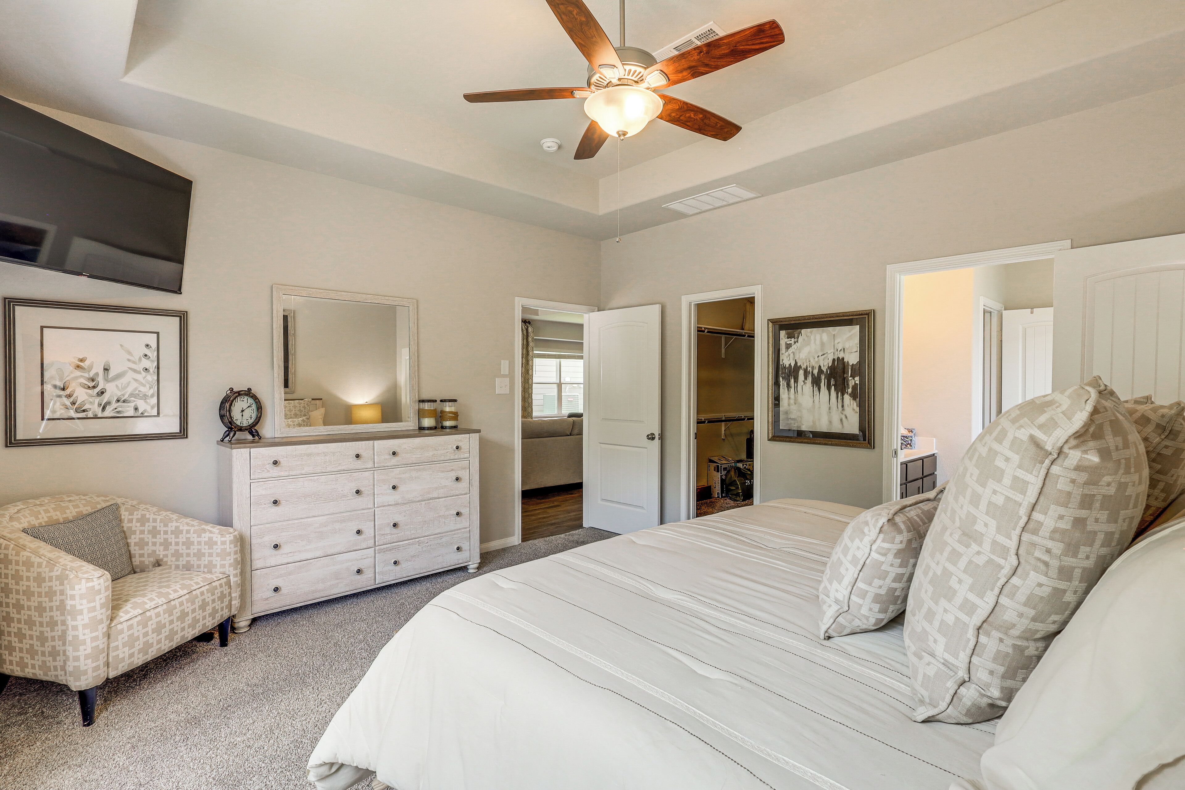 Une chambre à coucher avec un grand lit, un ventilateur de plafond, une commode, une chaise et un dressing.