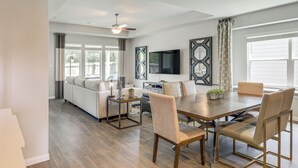 A modern living room with a dining area, a sofa set, a TV mounted on the wall, and a ceiling fan. - Walk to Brazos County Expo: Elegant Home w/ Grill! (Bryan)