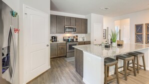 A modern kitchen with a central island, stainless steel appliances, and wooden cabinets. - Walk to Brazos County Expo: Elegant Home w/ Grill! (Bryan)