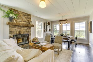 A living room with a stone fireplace, a dining area with a table and chairs, and large windows offering a view. - Lovely Country Retreat, 4 Mi to Dtwn Narrowsburg! (Narrowsburg)