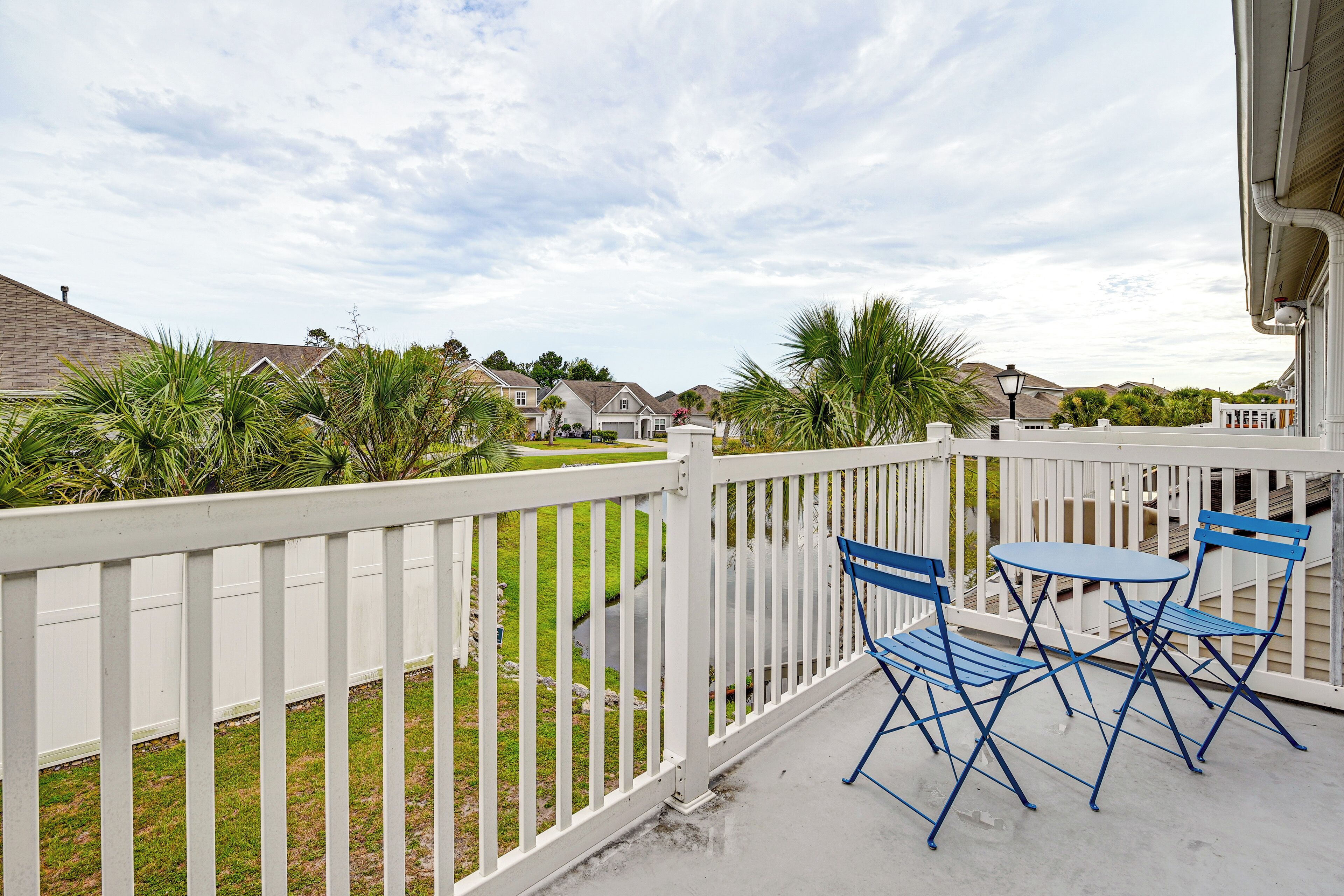 A balcony with a white railing, blue folding chairs, and a small table.