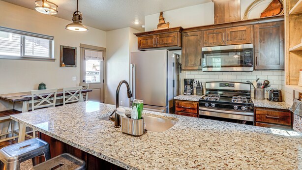 A kitchen with granite countertops, stainless steel appliances, wooden cabinets, and pendant lighting. - Charming Donnelly Home - 1 Mi to Lake Cascade! (Donnelly)